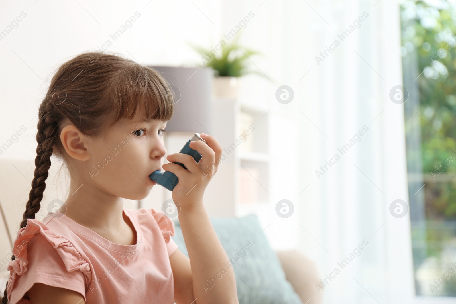 Photo of Little girl using asthma inhaler on blurred background