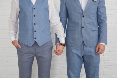 Photo of Newlywed gay couple holding hands near white wall, closeup