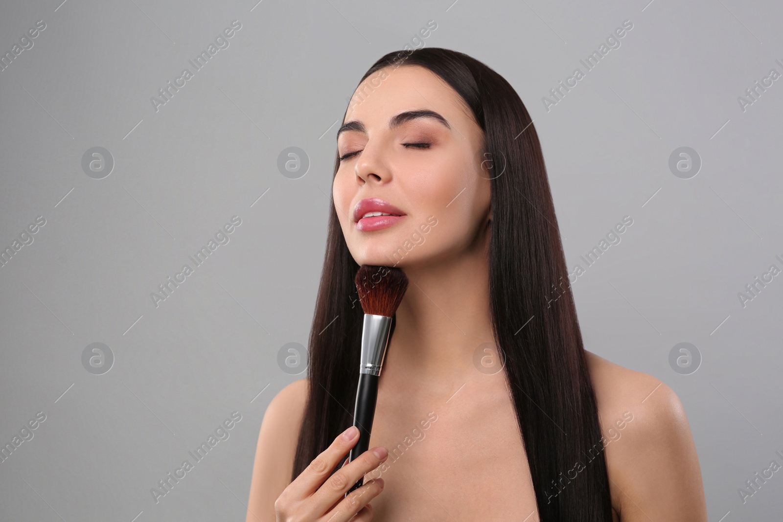 Photo of Beautiful woman with makeup brush on light grey background, space for text