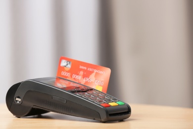 Photo of Modern payment terminal with credit card on table indoors. Space for text