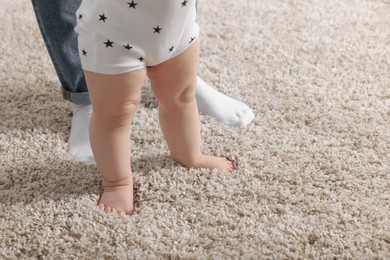 Photo of Mother supporting her baby son while he learning to walk on carpet, closeup. Space for text