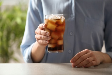 Photo of Woman holding glass of cola with ice at table, closeup