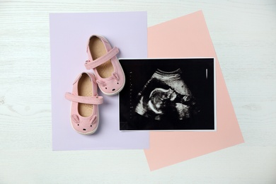 Ultrasound photo of baby and cute boots on wooden background, flat lay