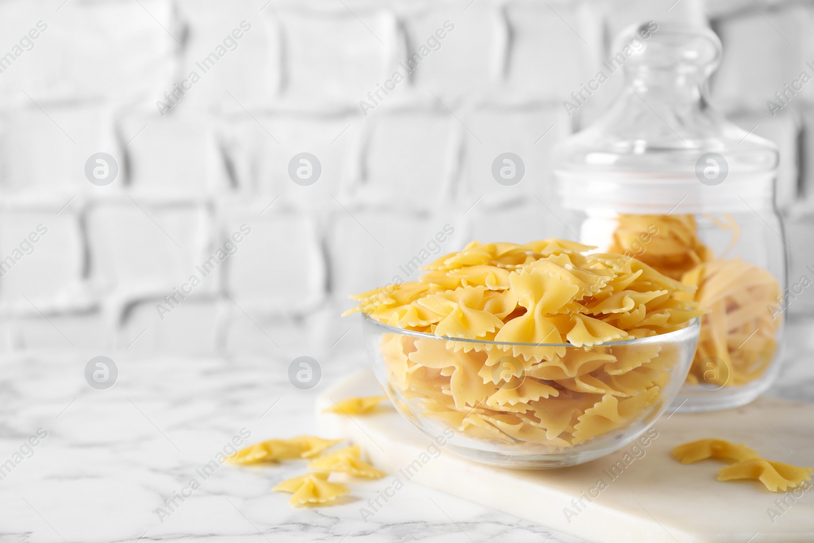 Photo of Raw pasta in bowl on white marble table, space for text