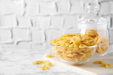 Raw pasta in bowl on white marble table, space for text