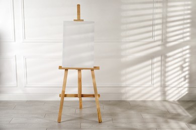 Photo of Wooden easel with blank canvas near light wall. Space for text