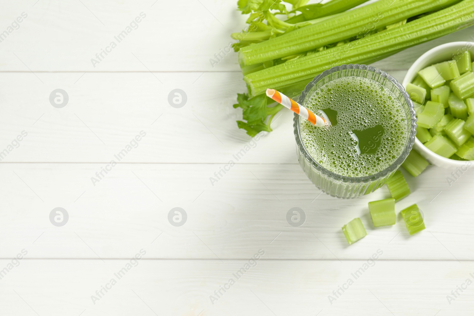 Photo of Glass of celery juice and fresh vegetables on white wooden table, flat lay. Space for text