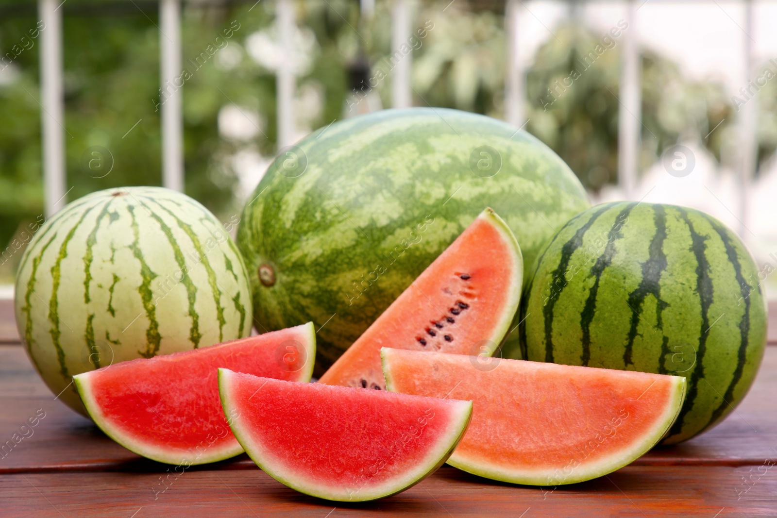 Photo of Different cut and whole ripe watermelons on wooden table outdoors