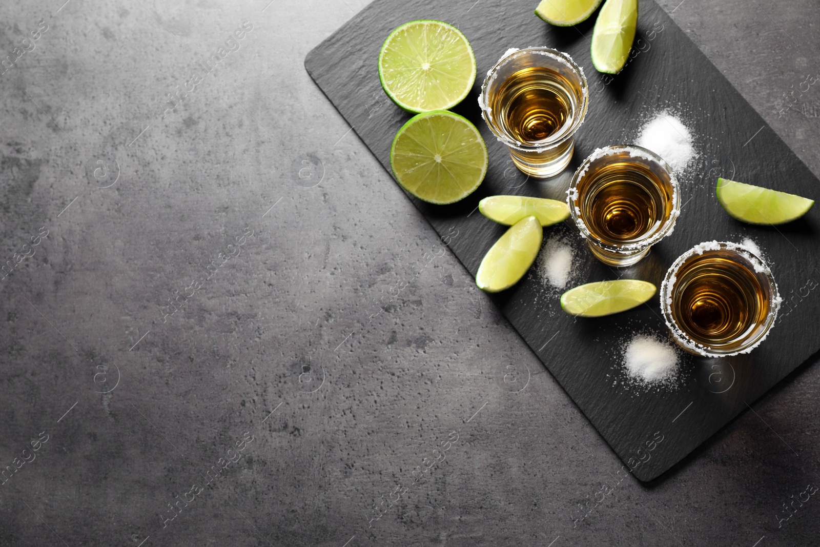 Photo of Mexican Tequila shots with salt and lime on grey table, top view. Space for text