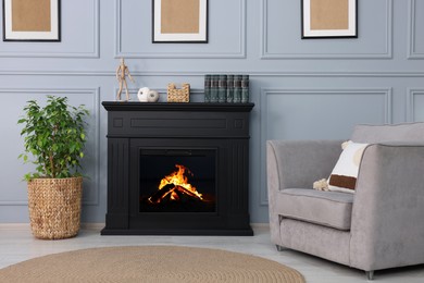 Photo of Black stylish fireplace near armchair and potted plant in cosy living room