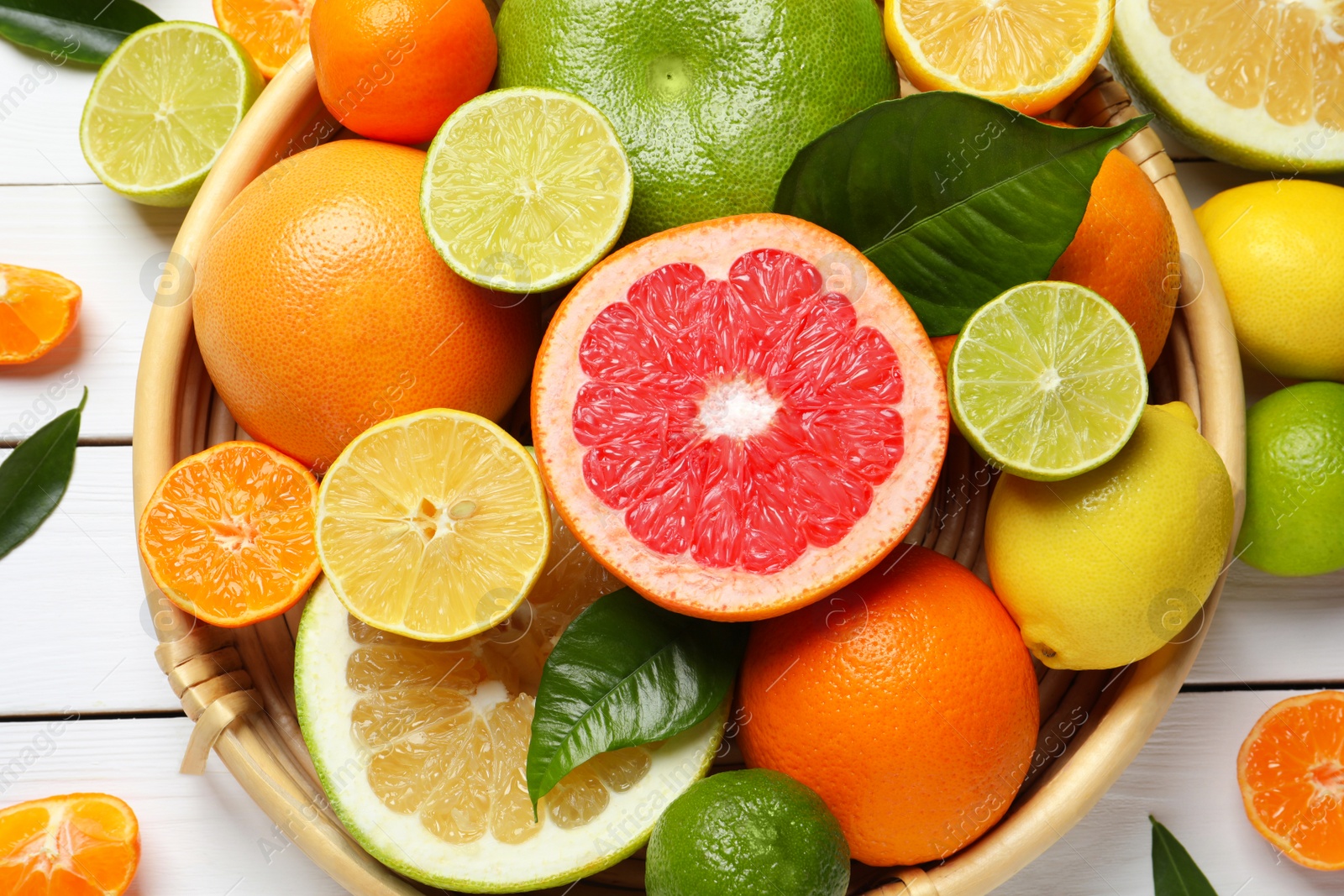 Photo of Different ripe citrus fruits with green leaves on white wooden table, flat lay