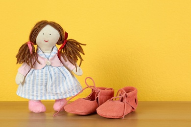 Photo of Doll and bootees for baby room interior on wooden table near yellow wall