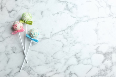 Different tasty cake pops on white marble background, flat lay. Space for text