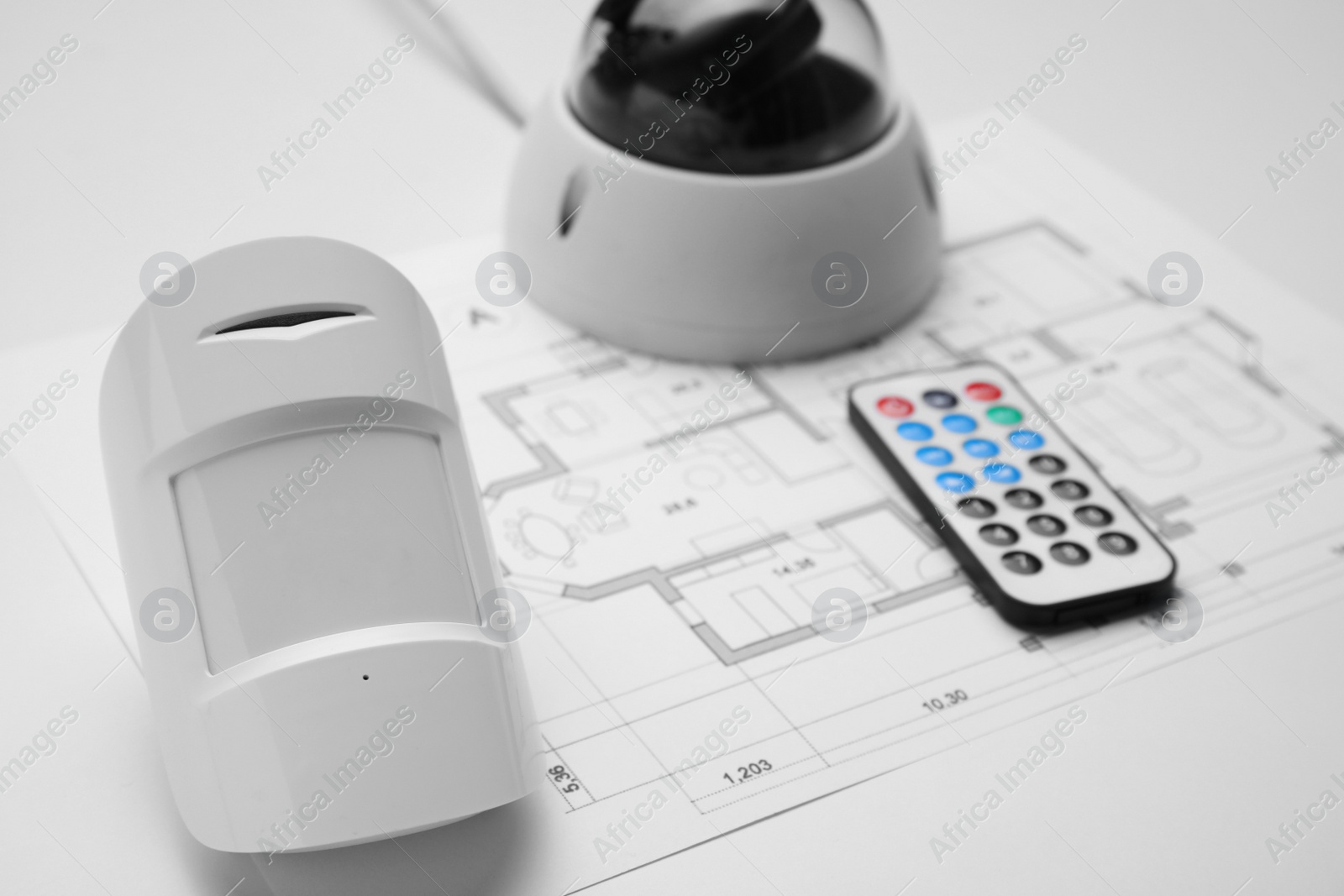 Photo of CCTV camera, remote control, movement detector and building plan on white background, closeup. Home security system