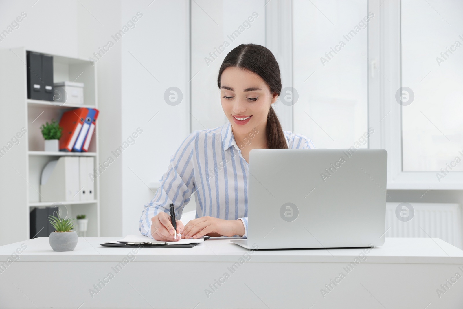 Photo of Young female intern working with laptop at table in office