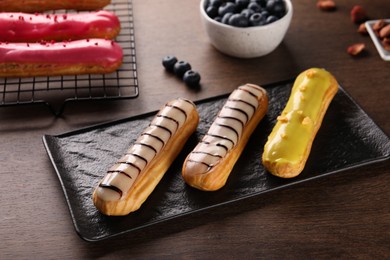 Different tasty glazed eclairs on wooden table, closeup