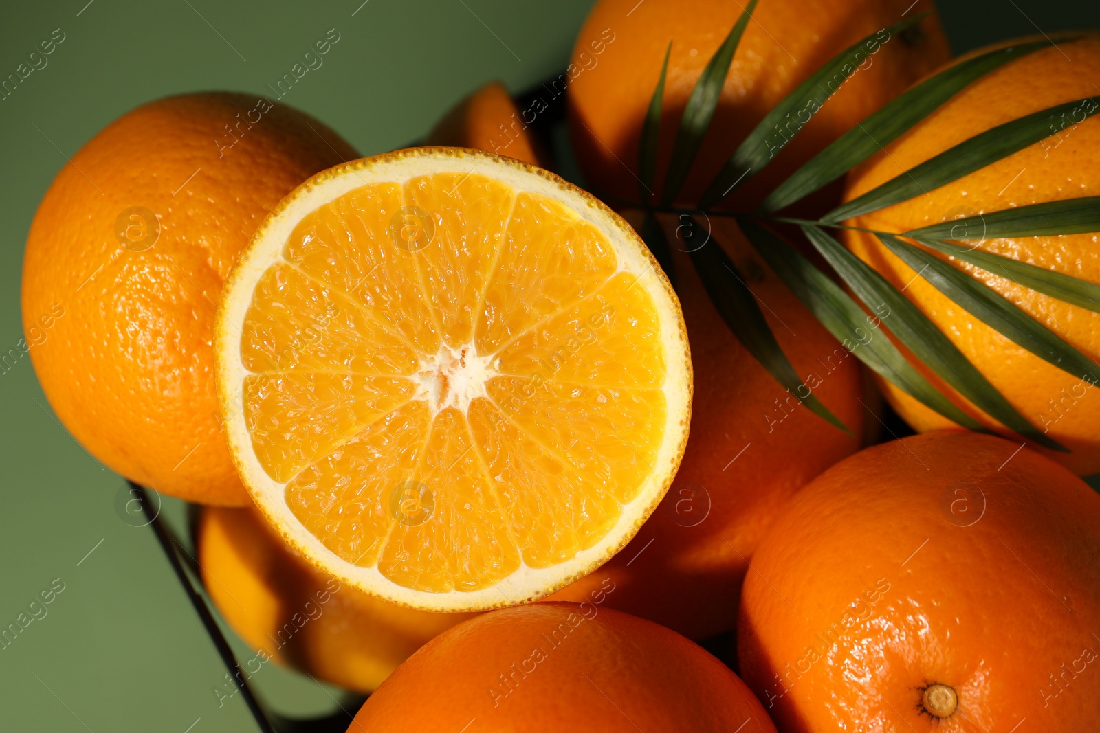 Photo of Fresh oranges in metal basket on green background, top view