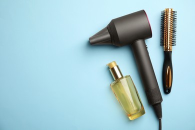 Photo of Hair care product, dryer and round brush on light blue background, flat lay. Space for text