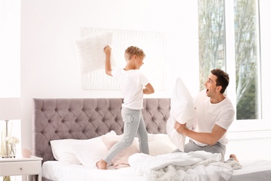 Photo of Father and son having pillow fight on bed at home