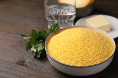 Photo of Raw cornmeal in bowl, butter and parsley on wooden table, closeup. Space for text