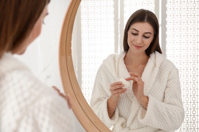 Photo of Young woman with face cream near mirror in bathroom