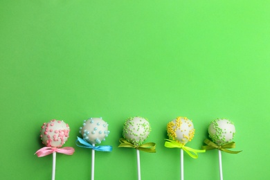 Different tasty cake pops on green background, flat lay. Space for text