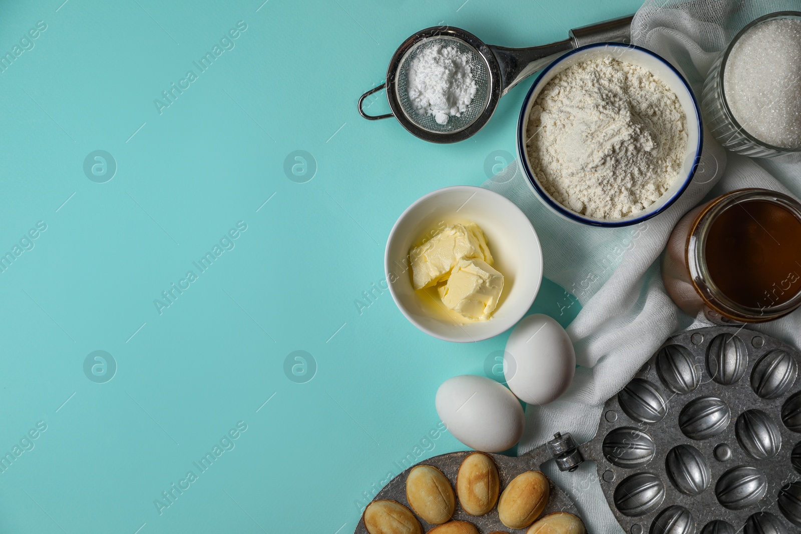 Photo of Freshly baked homemade walnut shaped cookies, baking dish and ingredients on light blue table, flat lay. Space for text