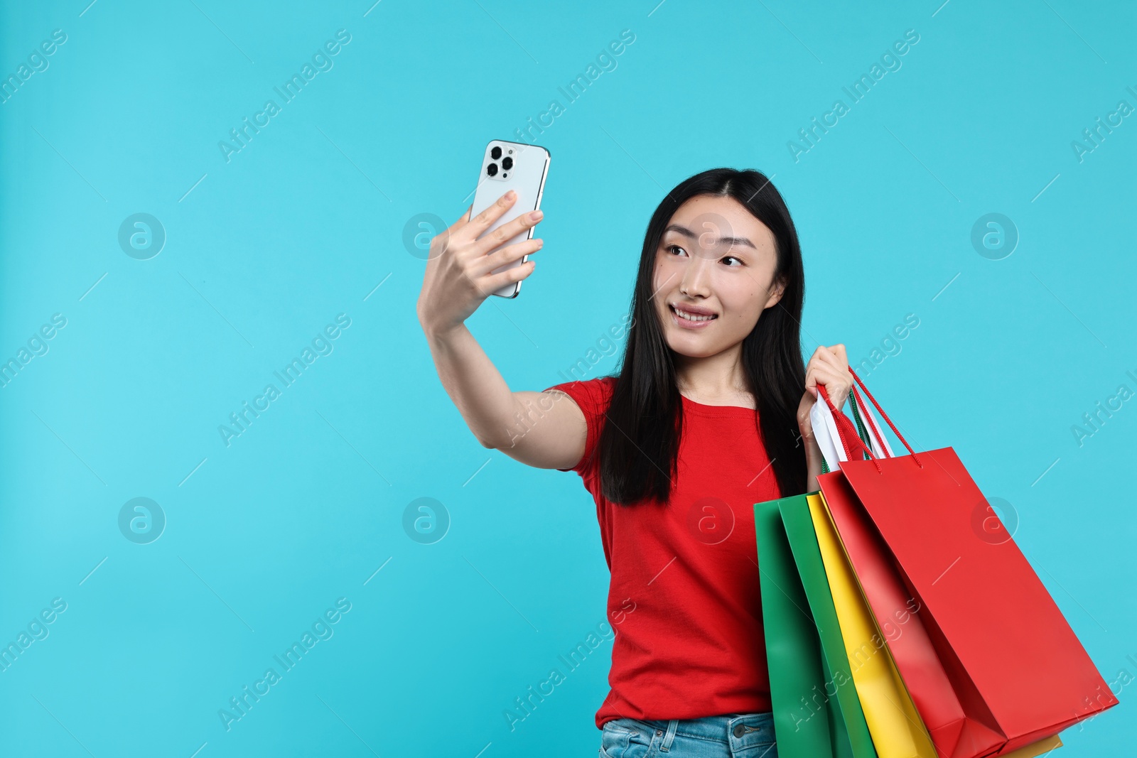 Photo of Smiling woman with shopping bags taking selfie on light blue background. Space for text