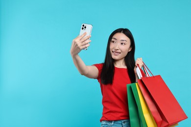 Smiling woman with shopping bags taking selfie on light blue background. Space for text