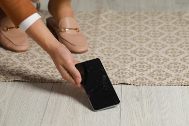 Photo of Woman taking damaged smartphone from floor, closeup. Device repairing