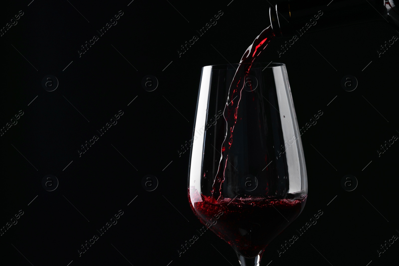 Photo of Pouring red wine into glass against black background, closeup. Space for text