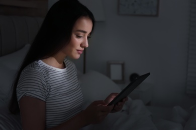 Photo of Happy woman using tablet in dark bedroom