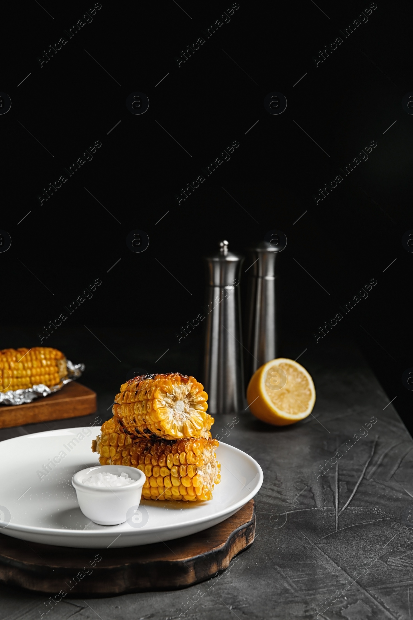 Photo of Plate with delicious grilled corn cobs and salt on gray table. Space for text