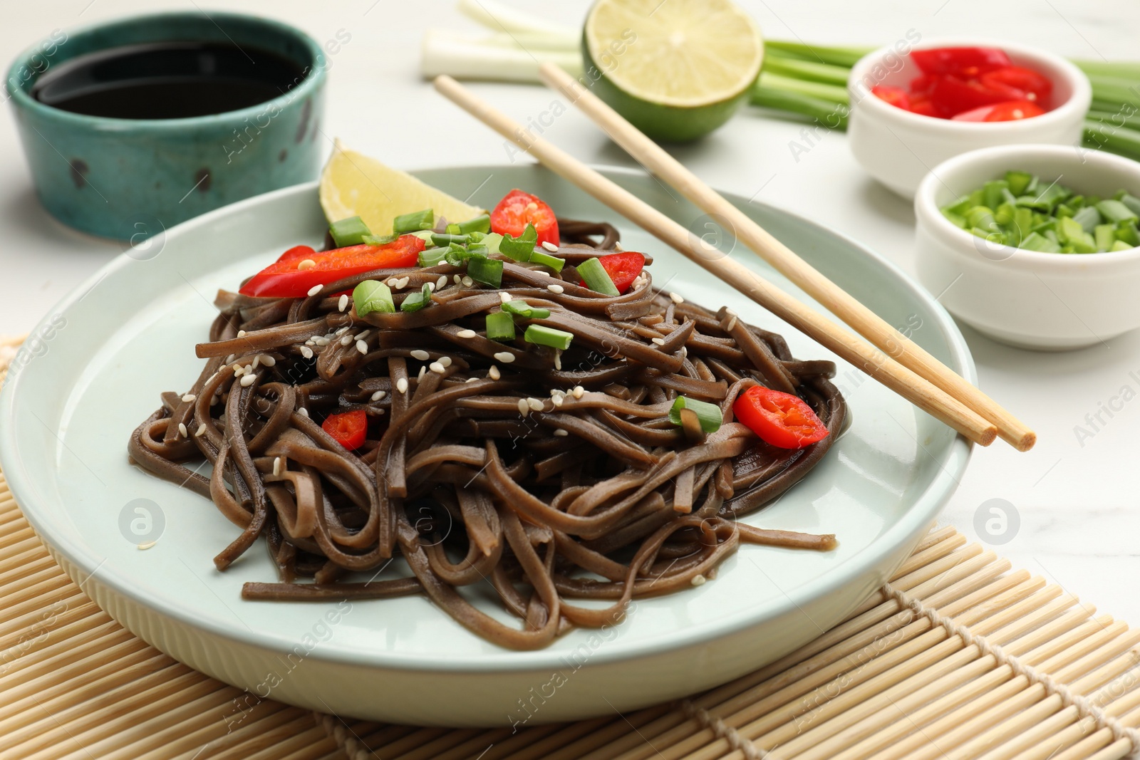 Photo of Tasty buckwheat noodles (soba) with chili pepper, onion and chopsticks on white table