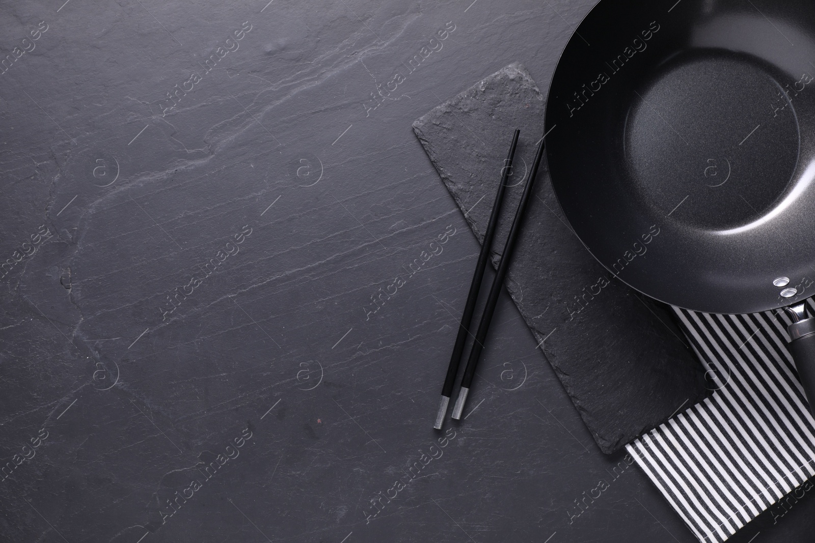 Photo of Empty iron wok and chopsticks on black table, top view. Space for text