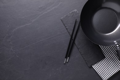 Empty iron wok and chopsticks on black table, top view. Space for text