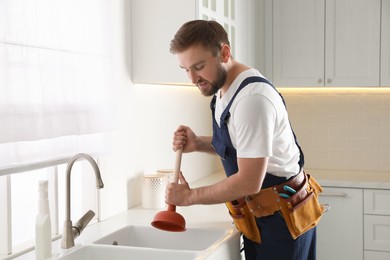 Photo of Plumber using plunger to unclog sink drain in kitchen