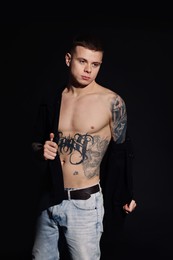 Photo of Young man with tattoos wearing black shirt on dark background