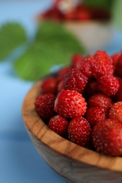 Fresh wild strawberries in bowl on light blue table, closeup