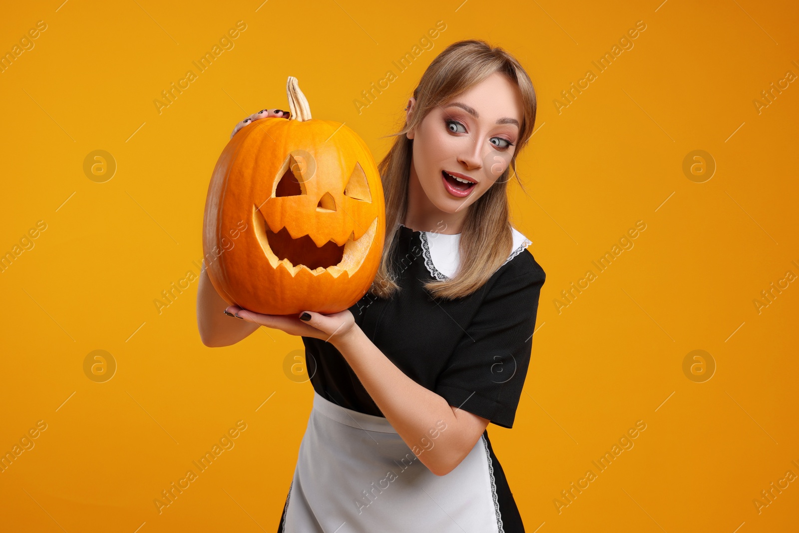 Photo of Emotional woman in scary maid costume with carved pumpkin on orange background. Halloween celebration