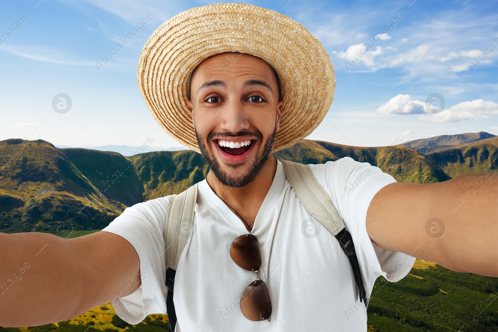 Image of Smiling young man in straw hat taking selfie in mountains