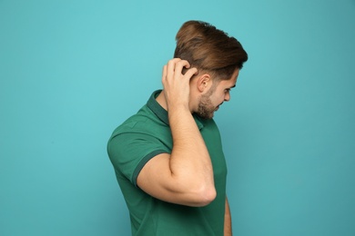 Young man scratching head on color background. Annoying itch