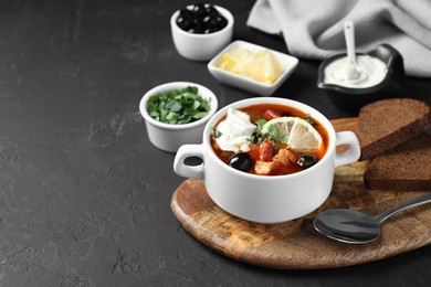 Photo of Meat solyanka soup with sausages, olives and vegetables in bowl served on dark grey textured table, space for text