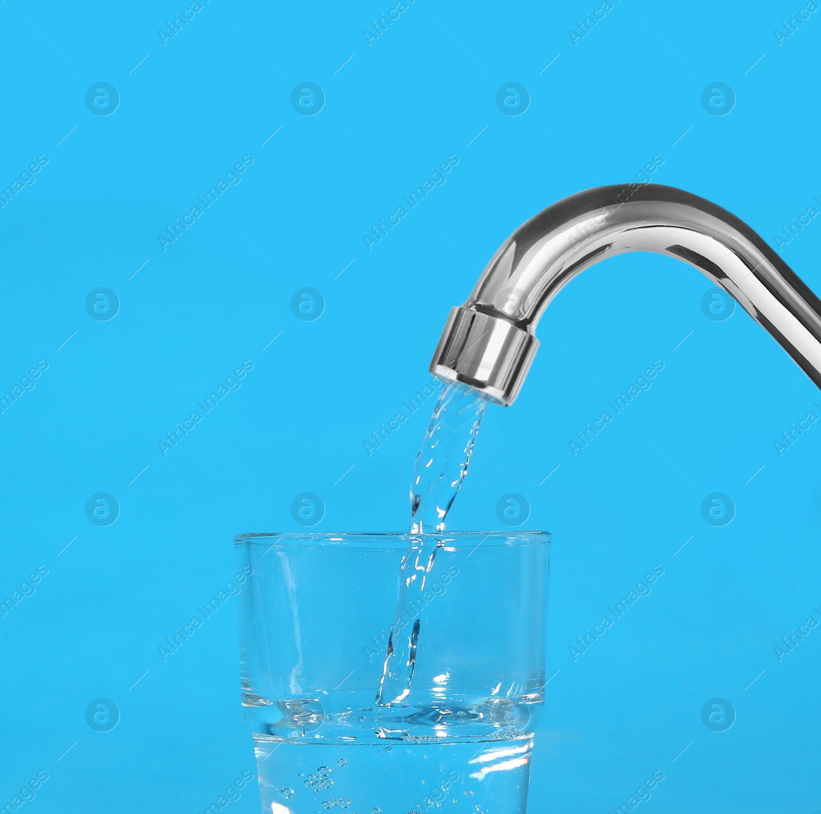 Image of Filling glass with water from tap on light blue background