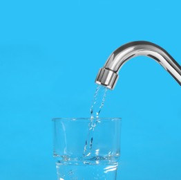 Image of Filling glass with water from tap on light blue background