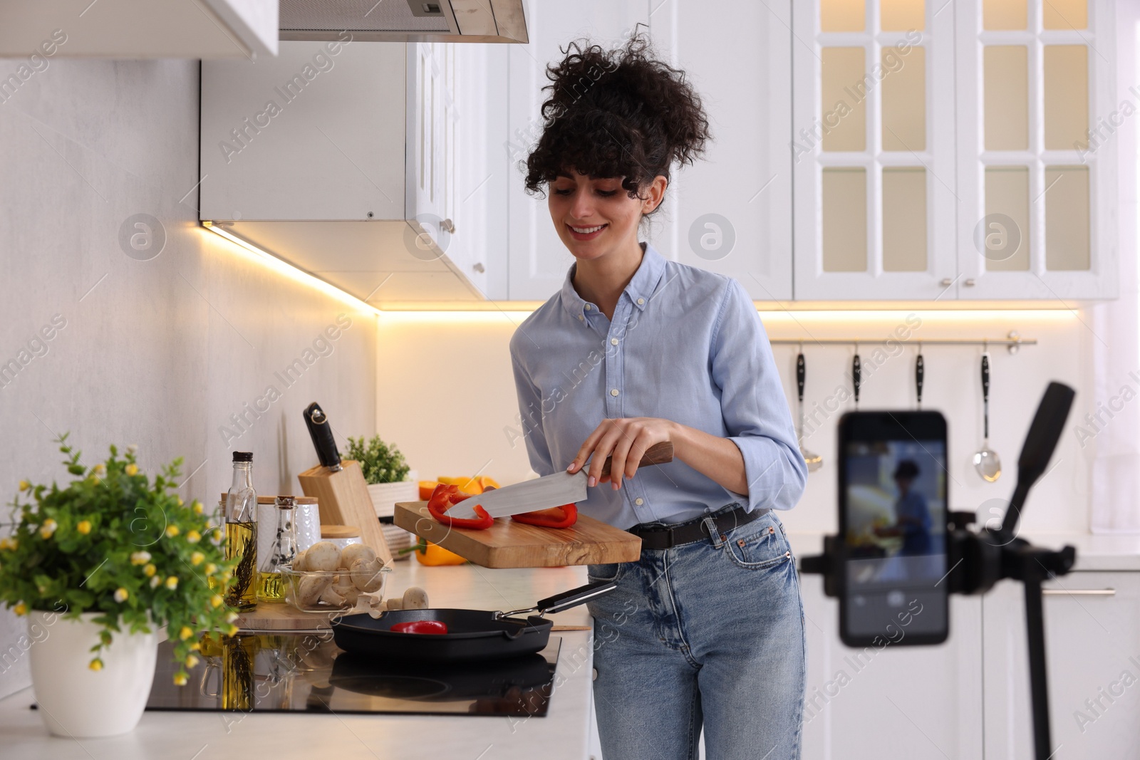 Photo of Smiling food blogger cooking while recording video in kitchen