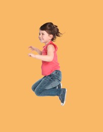 Happy cute girl jumping on pale orange background