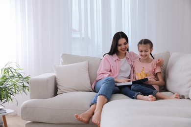 Photo of Mother and daughter with book on sofa in living room=