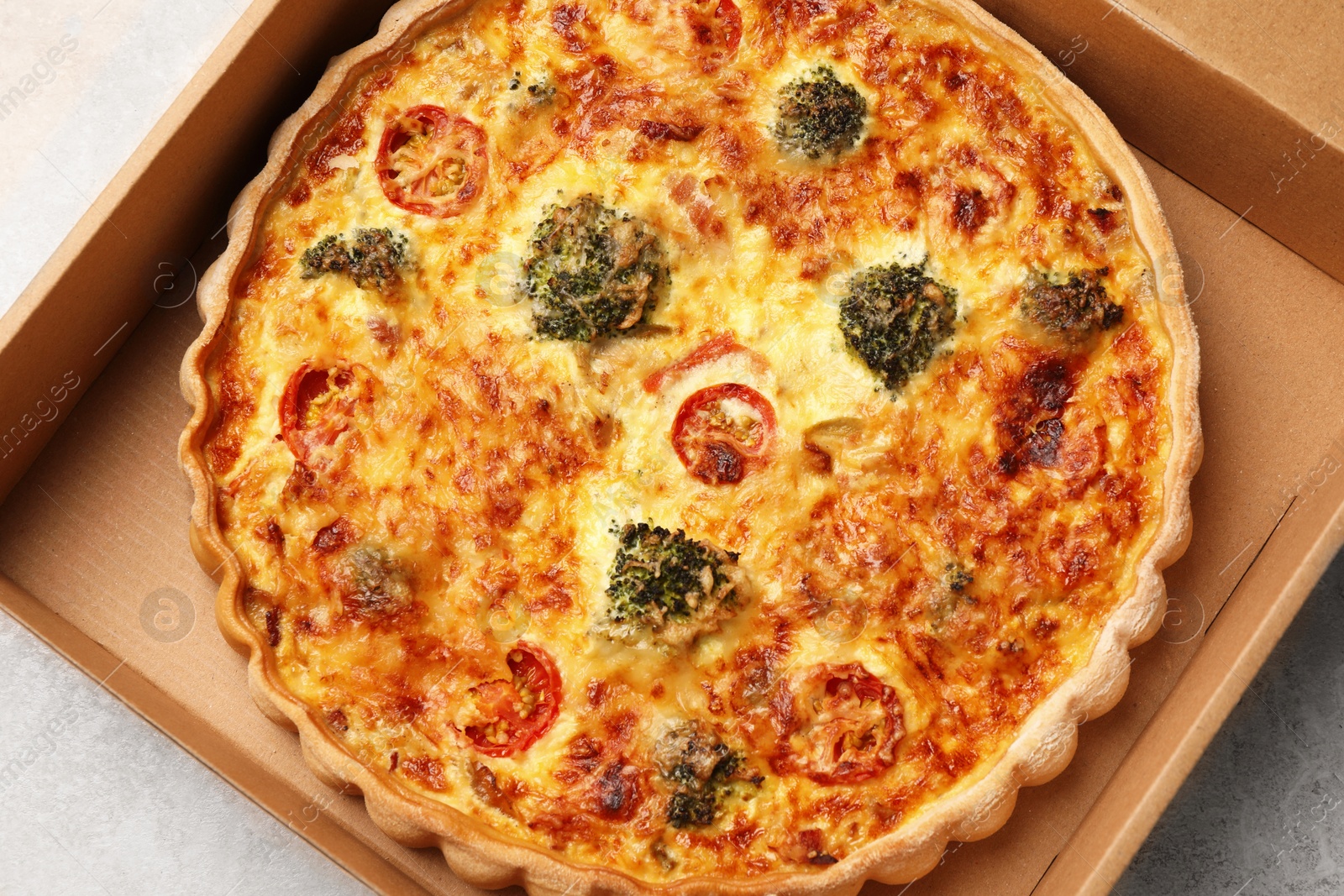 Photo of Delicious homemade vegetable quiche in carton box on light gray table, top view