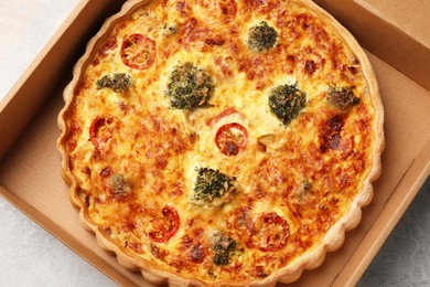Photo of Delicious homemade vegetable quiche in carton box on light gray table, top view